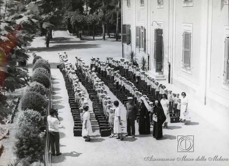 Bambini e bambine radunati in cortile con suore e responsabili delle colonie