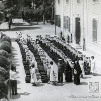 Bambini e bambine radunati in cortile con suore e responsabili delle colonie